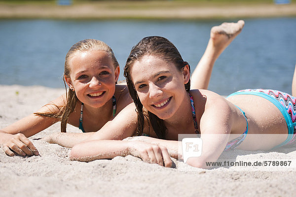 Two smiling girls in bikinis lying at bathing lake