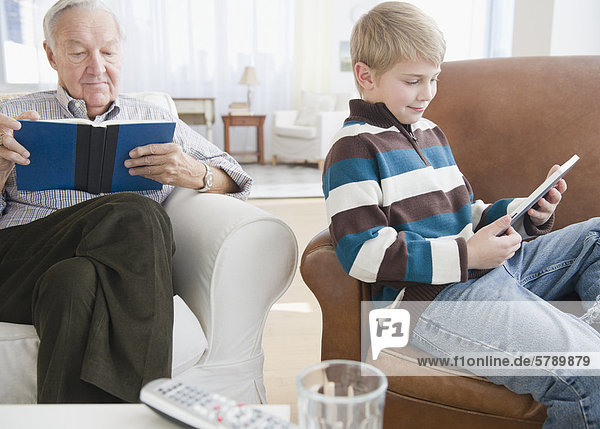 Grandfather reading book  grandson (8-9) reading e-book in living room