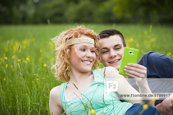 Junges Paar liegt auf einer Wiese mit einem Smartphone