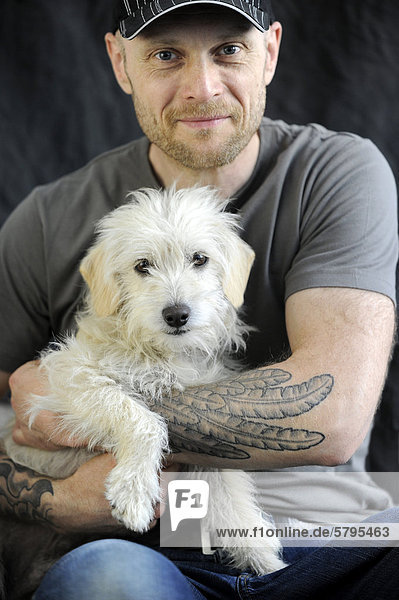 Mongrel terrier  one year  in the arms of its tattooed owner
