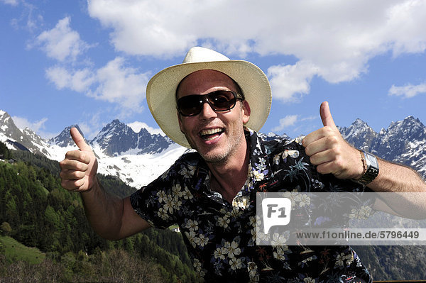 Smiling man wearing a straw hat  sunglasses  thumbs up  in the Tyrolean mountains  Kaunertal  Tyrol  Austria  Europe