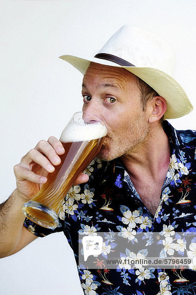 Mann mit Strohhut und Hawaiihemd trinkt aus einem Glas Weizenbier