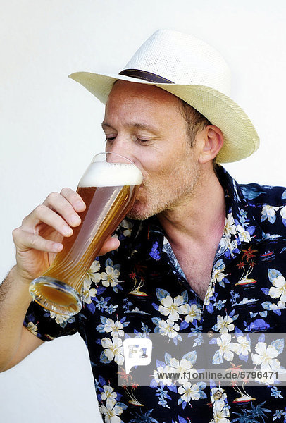 Mann mit Strohhut und Hawaiihemd trinkt aus einem Glas Weizenbier