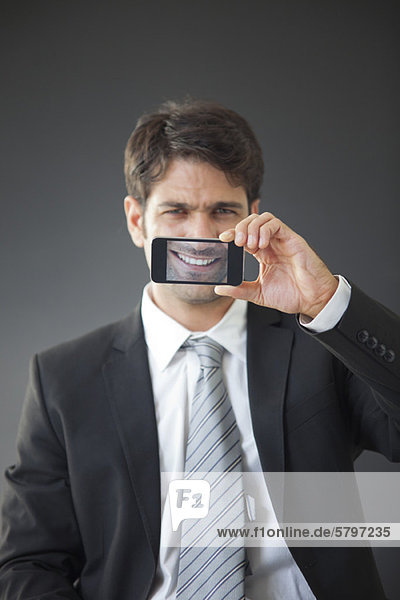 Mann hält das Smartphone hoch und zeigt das Bild seines eigenen Lächelns.
