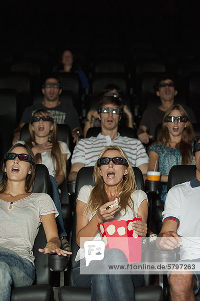 Audience wearing 3-D glasses in movie theater with shocked expressions on faces