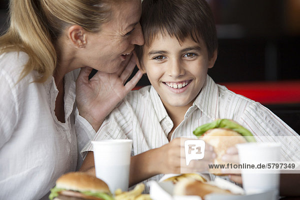 Mutter flüstert in das Ohr des Sohnes im Fastfood-Restaurant