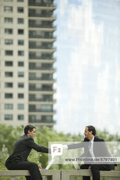 Business executives sitting outdoors with laptop computers  shaking hands
