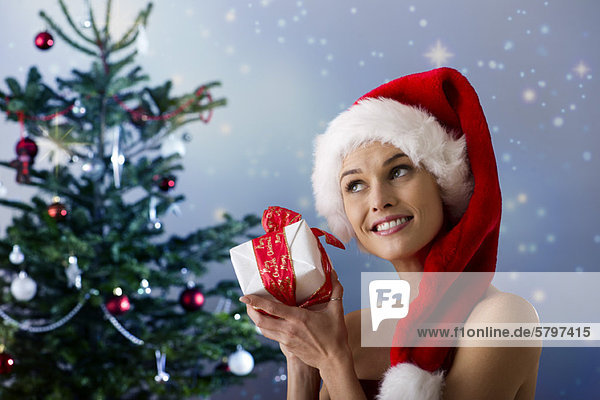 Frau mit Weihnachtsmütze  schüttelndes Weihnachtsgeschenk