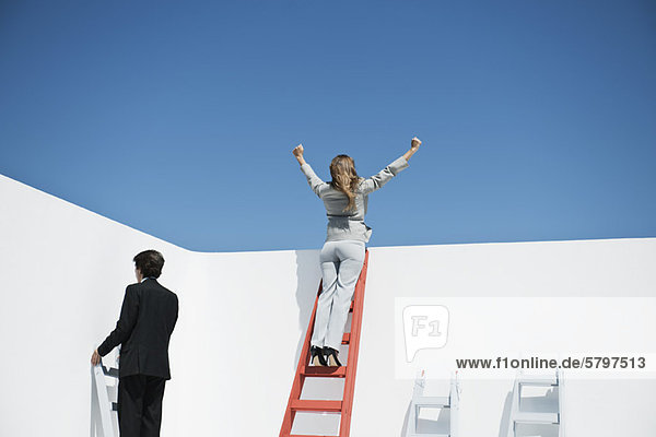 Geschäftsfrau steht oben auf der Leiter mit in die Luft erhobenen Armen