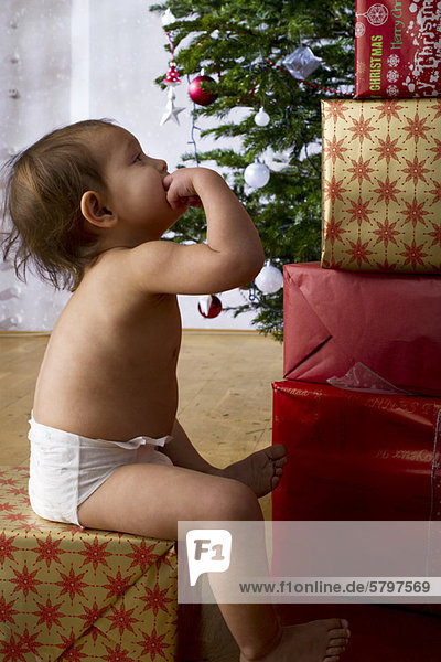 Kleines Mädchen  das über einen hohen Stapel Weihnachtsgeschenke nachdenkt.