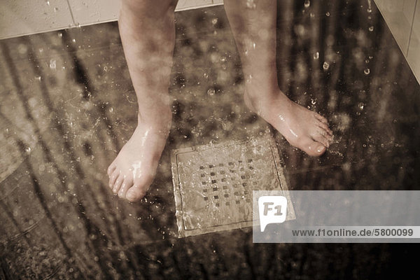 Niedriger Abschnitt eines Jungen der im häuslichen Badezimmer am Abfluss steht.