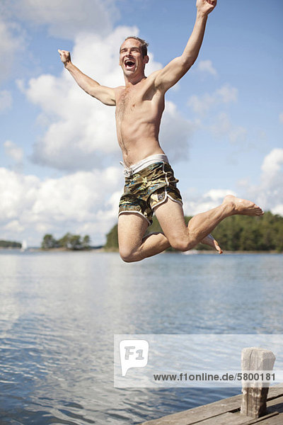 Excited mature man jumping into lake