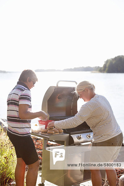 Zwei Personen kochen auf einem Campingkocher in der Nähe des Sees.