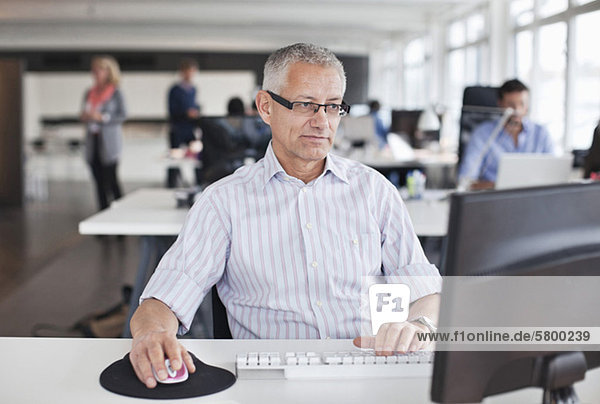 Businessman using computer in office with colleagues in background
