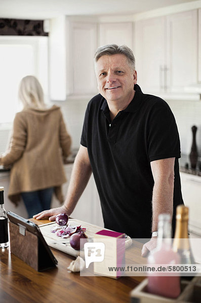 Porträt eines lächelnden reifen Mannes in der Küche mit Frau im Hintergrund