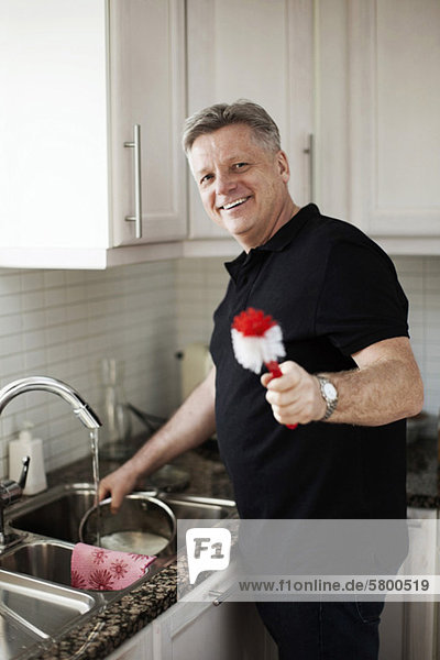 Porträt eines lächelnden reifen Mannes mit Bürste in der Küche