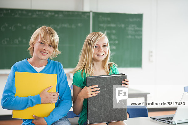 Zwei lächelnde Schüler im Klassenzimmer mit Aktenordnern