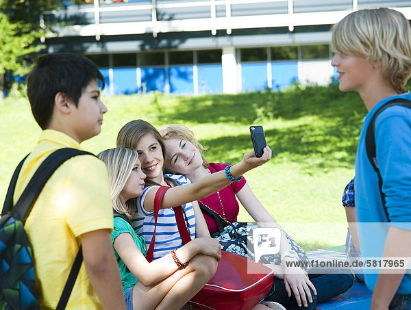 Mädchen auf einer Bank mit einem Handy und zwei Jungen