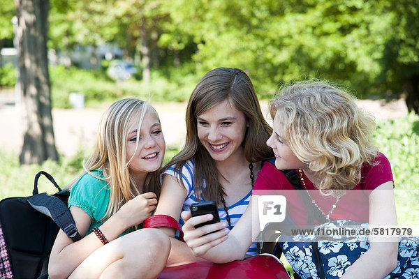 Drei lächelnde Teenagerinnen mit Handy
