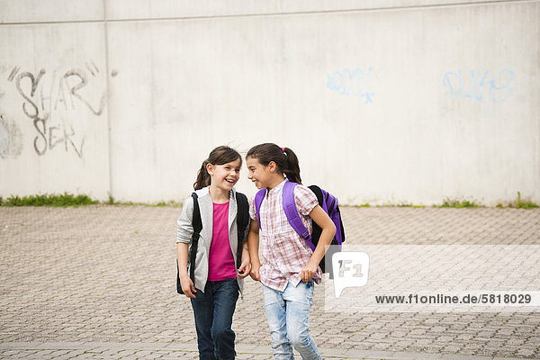 Zwei lächelnde Mädchen gehen über den Schulhof