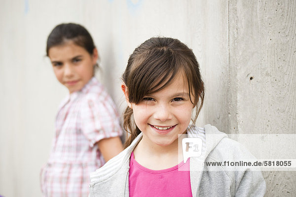 Lächelndes Mädchen lehnt an einer Betonwand