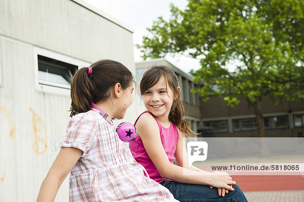 Zwei lächelnde Mädchen sitzen auf dem Schulhof