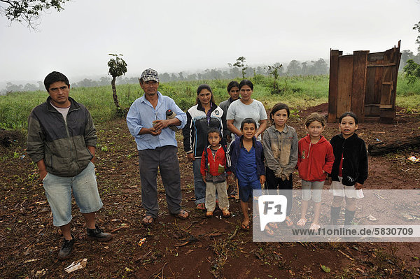 Landgrabbing: Kleinbauernfamilie  die von Investoren von ihrem Land vertrieben wurde und jetzt in einer provisorischen Hütte am Straßenrand lebt  hinten das Sojafeld eines Großgrundbesitzers auf ihrem ehemaligen Land  Landgrabbing  Distrikt Carlos Antonio Lopez  Provinz Itapua  Paraguay  Südamerika