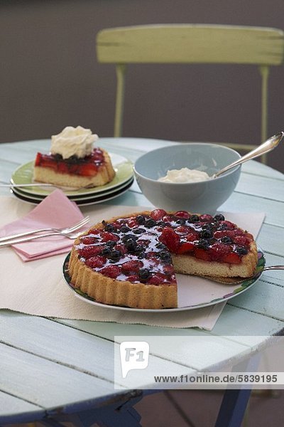 Erdbeer-Heidelbeer-Kuchen mit Sahne auf Gartentisch