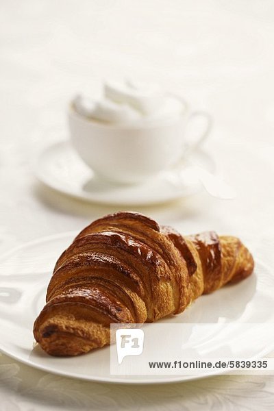 Ein Croissant auf Teller  im Hintergrund ein Cappuccino
