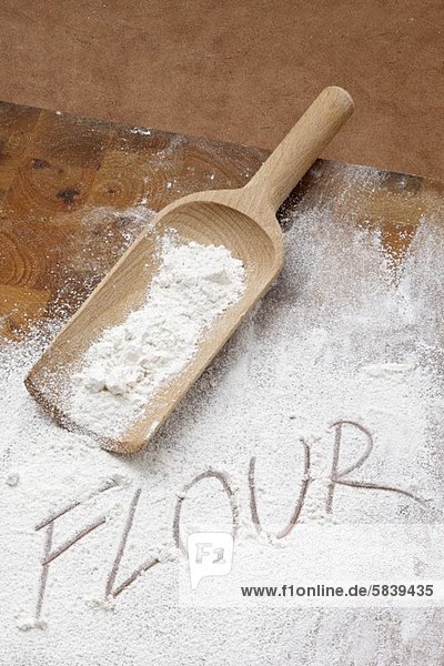 The word FLOUR written in flour with a wooden scoop
