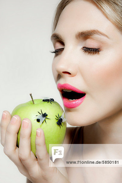 Junge Frau isst Apfel mit Fliegen darauf