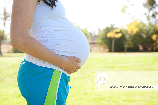 Schwangere junge Frau berührt den Bauch  Seitenansicht