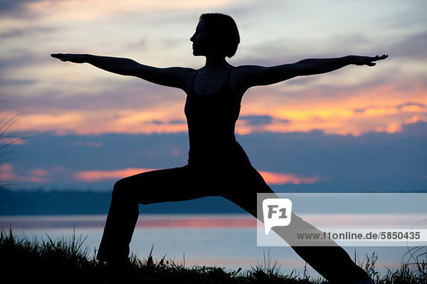 Silhouette der Frau in Krieger-Yoga-Pose bei Sonnenuntergang