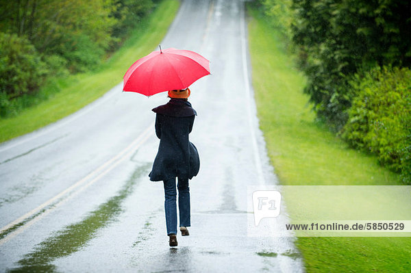 Frau auf leerer Straße mit rotem Regenschirm