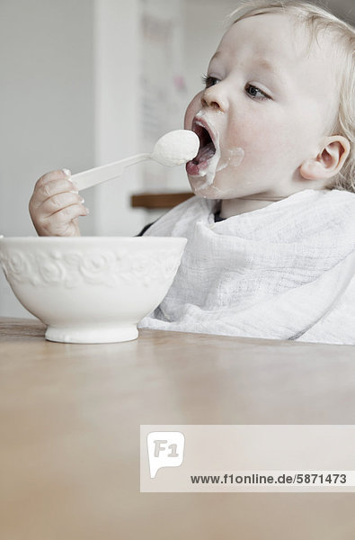 Junge  15 Monate  mit Lätzchen  isst mit Löffel einen Joghurt