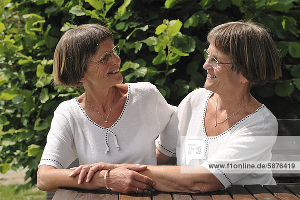 Zwei rüstige Zwillingsschwestern sitzen an einem Gartentisch