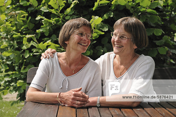 Zwei rüstige Zwillingsschwestern sitzen an einem Gartentisch