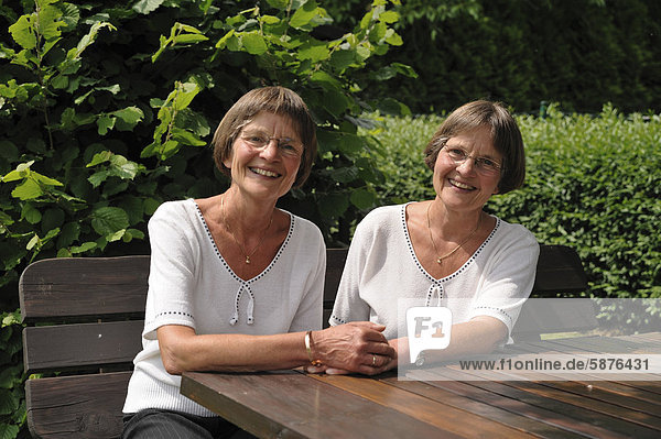 Zwei rüstige Zwillingsschwestern sitzen auf einer Gartenbank
