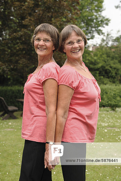 Zwei rüstige Zwillingsschwestern stehen Rücken an Rücken