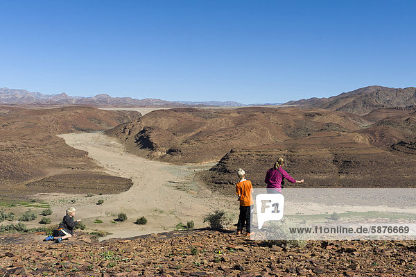 Father and son in a stone-throwing competition  view across the Oranje River from a viewpoint west of Aussenkehr  Richtersfeld National Park in South Africa at back  Namibia  Africa
