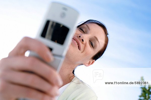 Low angle view of a young woman smiling and holding a mobile phone