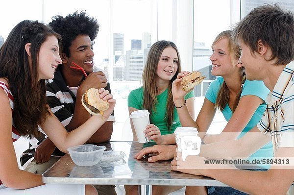Close_up of two young men and three young women sitting in a restaurant and smiling