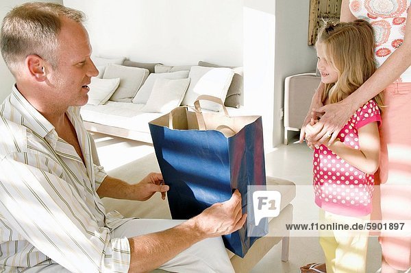 Close_up of a mature man holding a shopping bag and a girl standing with her mother in front of him