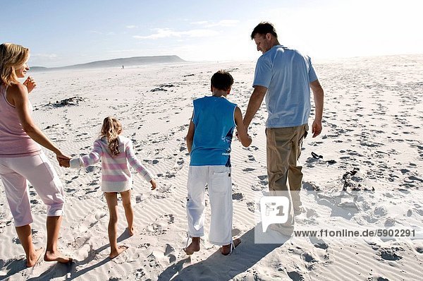 Rear view of a mid adult couple holding their childrens hands and running on the beach