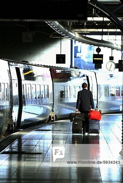 Rear view of a man pulling suitcases at a railroad station platform. Rear view of a man pulling suitcases at a railroad station platform