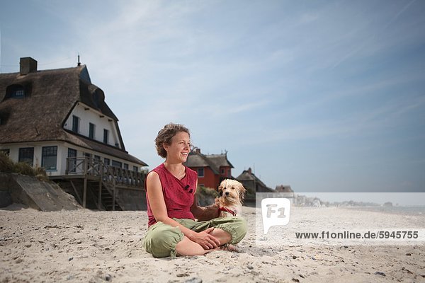 Frau sitzt mit Hund am Strand in Graswarder  Schleswig-Holstein  Deutschland