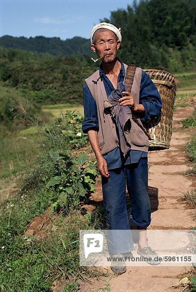 Porträt von ein Bauer mit Pfeife  typische weiße Stirnband tragen ein Weidenkorb  in Sichuan  China  Asien