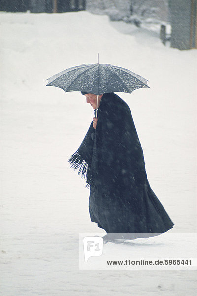 Alte Frau mit Schal und Sonnenschirm  Wandern im Schnee im winter