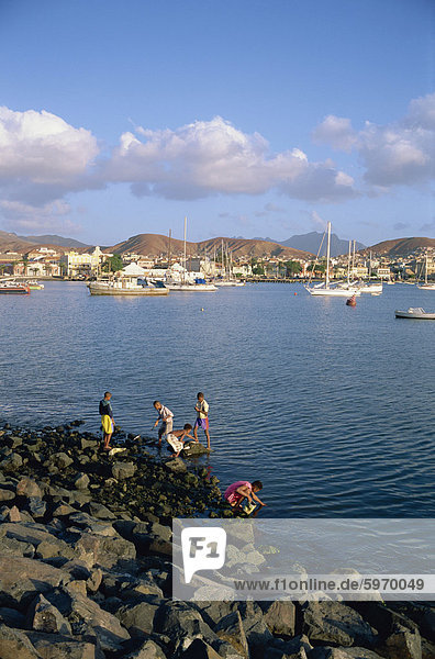 Boys on the rocks  with the harbour and town in the background  at Mindelo  Sao Vicente Island  Cape Verde Islands  Atlantic  Africa