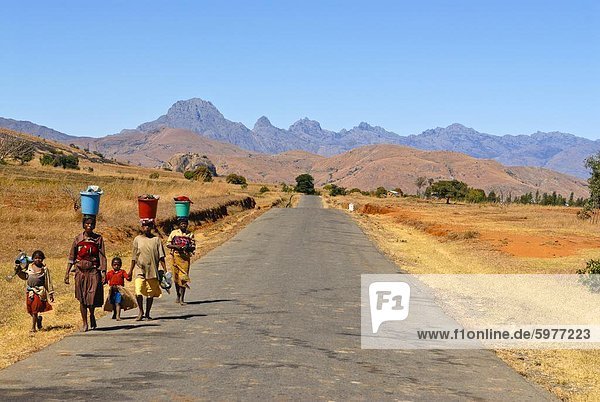 Menschen zu Fuß entlang einer Straße im Hintergrund Pic Bobby (Pic d'Imarivolanitra) im Andringitra Nationalpark  Madagaskar  Afrika